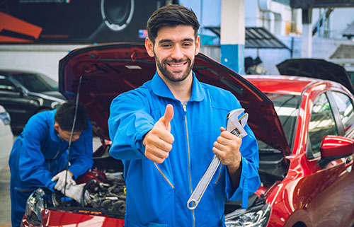 Certified mobile mechanic in Albuquerque holding a wrench and giving a thumbs up at an auto repair shop